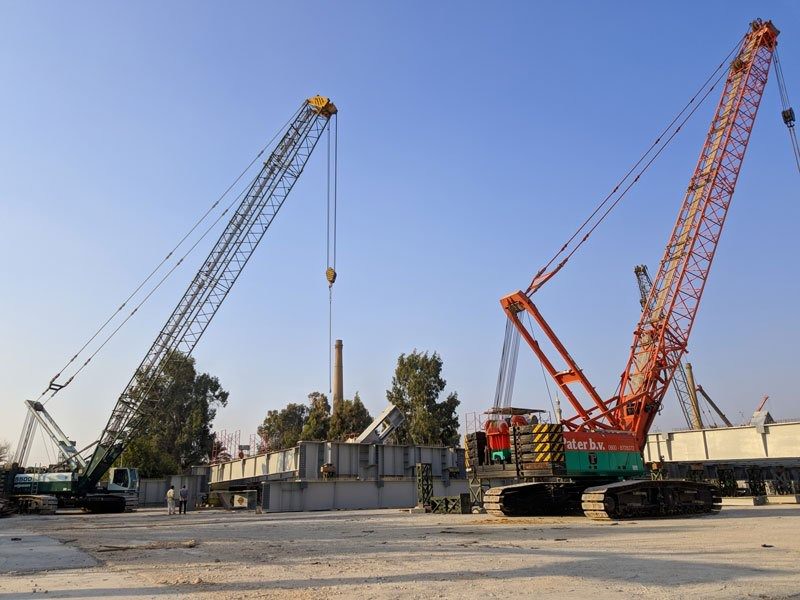 Two crawler cranes lifting together at a heavy construction site