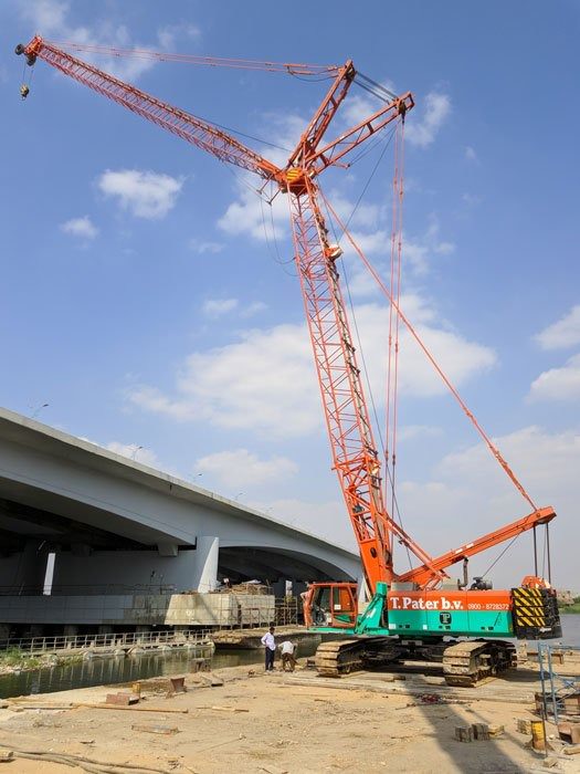 Crawler crane working beside a canal near a bridge construction site